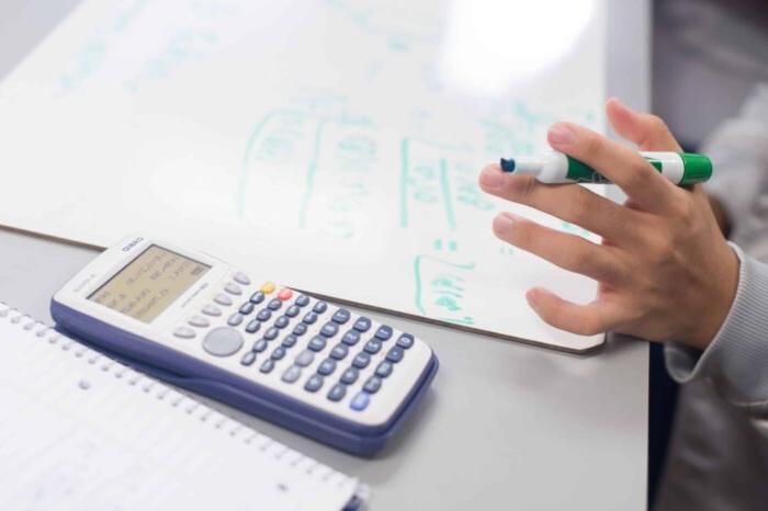 Image of calculator and someone holding a marker.