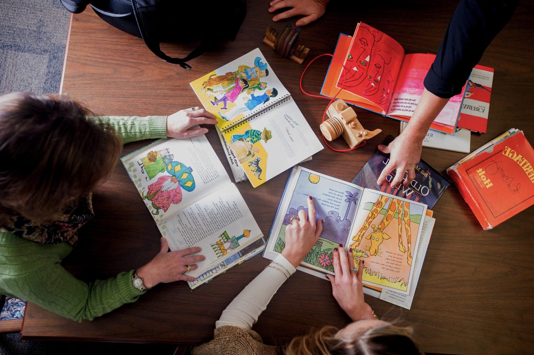 On top view of three people looking over children's book places on a desk.